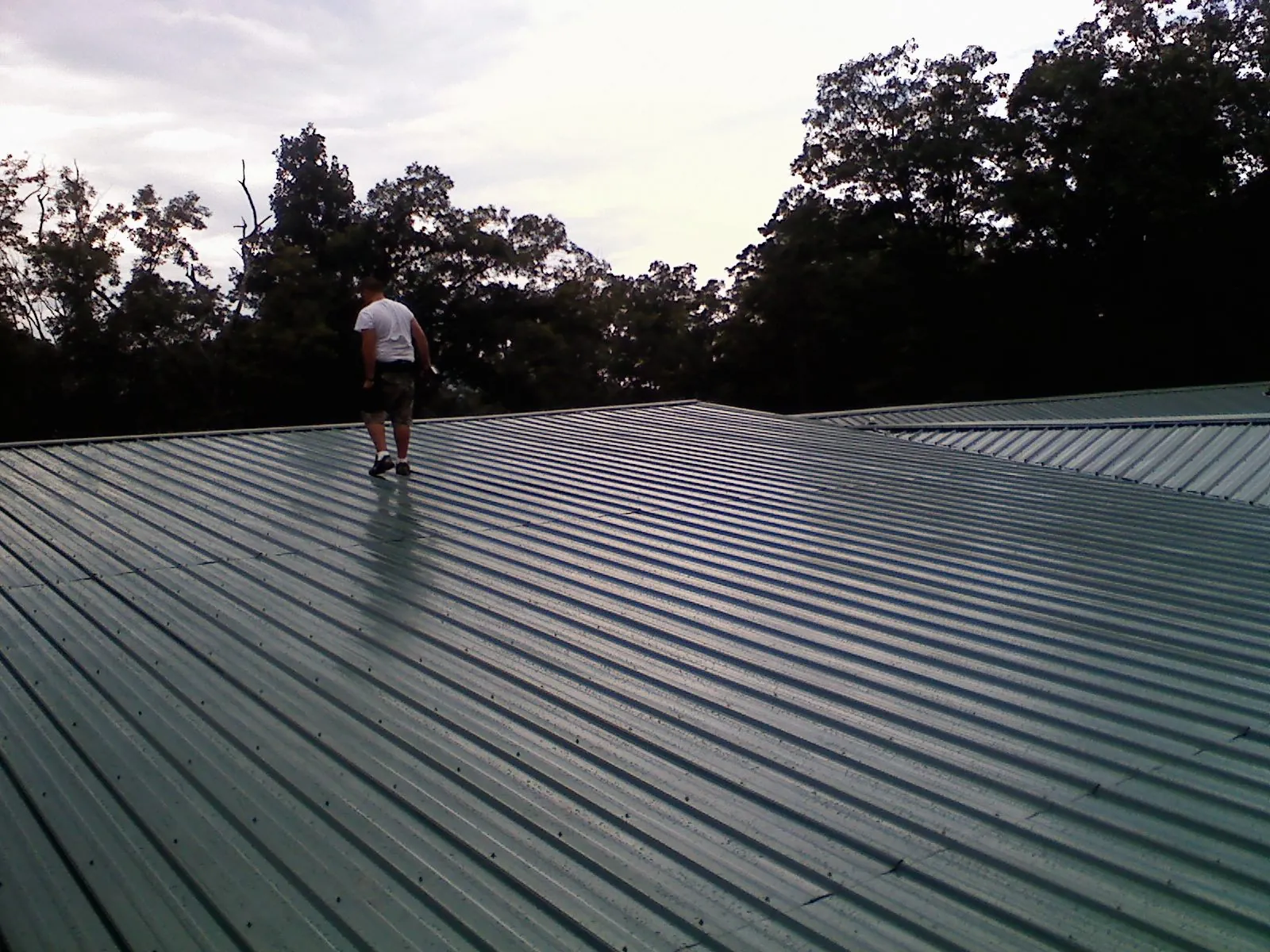 Roofer walking a wide expanse of new green metal roofing in Monroe
